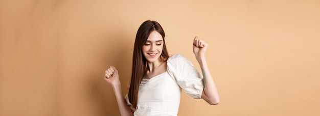 Free Photo carefree woman dancing and having fun close eyes and smiling standing on beige background