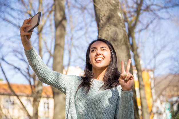 Free photo carefree woman grimacing and taking selfie photo outdoors