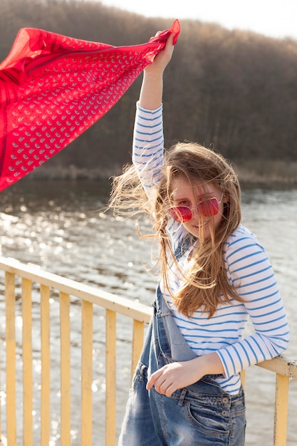 Free Photo carefree woman holding scarf in the wind by the lake