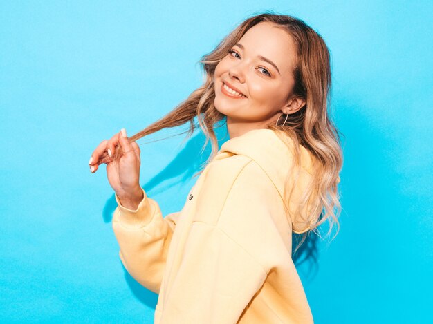 carefree woman posing near blue wall in studio. Positive model having fun.Touches her hair