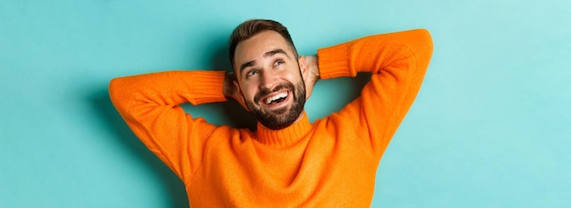 Free photo carefree young man daydreaming resting with hands behind head and looking at upper left corner happy