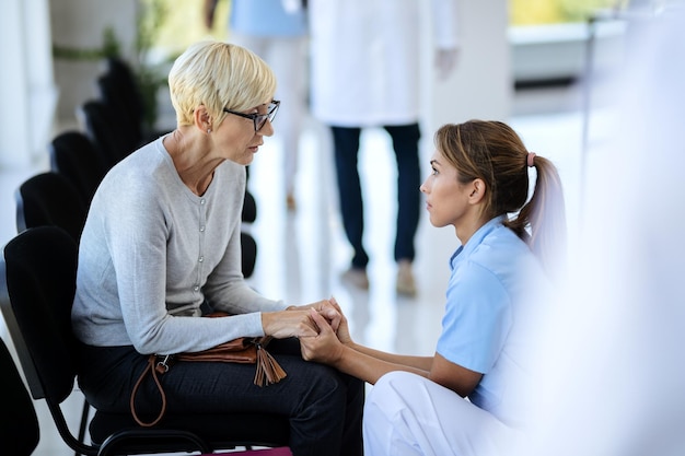 Caring nurse consoling mature woman in waiting room at medical clinic