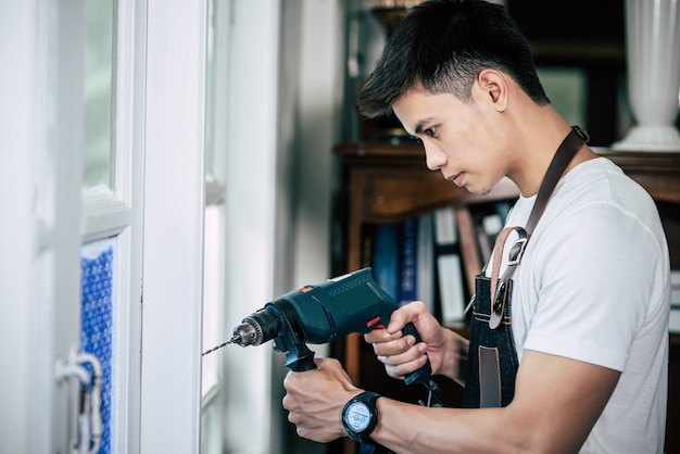 The carpenter holds the drill and drills the window.