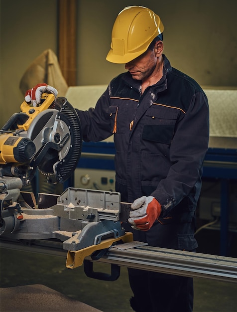 Free photo carpenter male dressed in a safety yellow cap works with chain-saw in a garage.