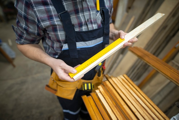 Free photo carpenter taking measurements of the plank he is about to cut in woodworking workshop