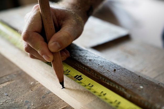 Free photo carpenter using pencil and measurement tape on wood