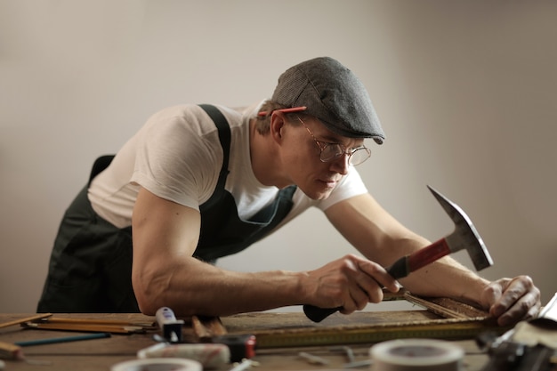 Carpenter wearing a white hard hat working with a hammer and screws trying to fix a wooden table