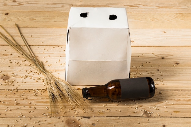 Carton box; beer bottle and ears of wheat on wooden surface