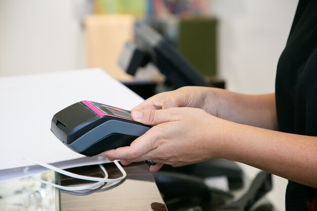 Cashier or seller operating payment process with pos terminal and credit card. Cropped shot, closeup of hands. Shopping or purchase concept