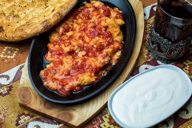 Cast iron platter of egg and tomato dish served with yogurt and tandoor bread