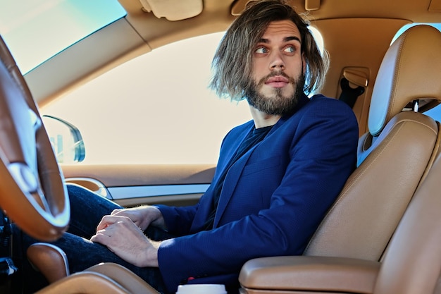 Free photo casual bearded male with long hair in a car.