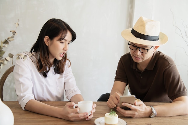 Casual man and woman talking happily while drink coffee and looking mobile phone 