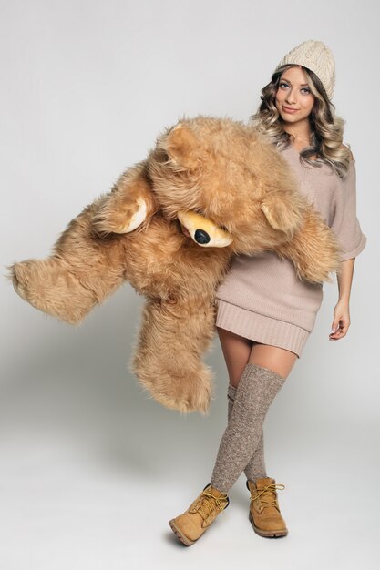 Casual smiling young woman in knitted clothes holding big soft teddy bear