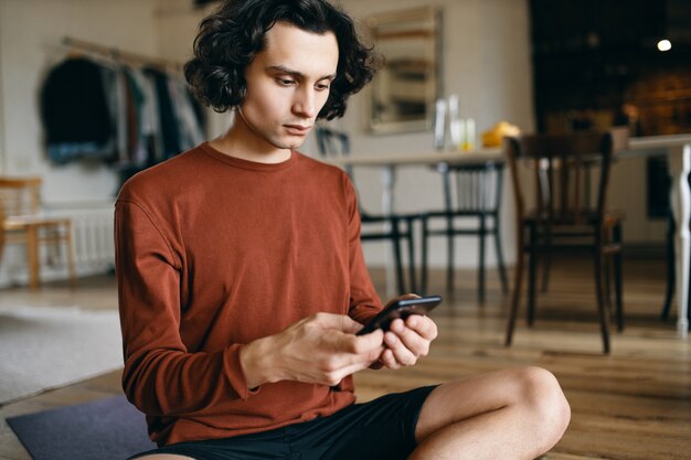 Casually dressed serious young businessman holding mobile texting sms or checking email while working remotely from home.