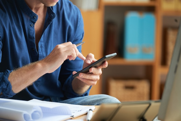 Casually dressed unrecognizable man using smartphone at work in office