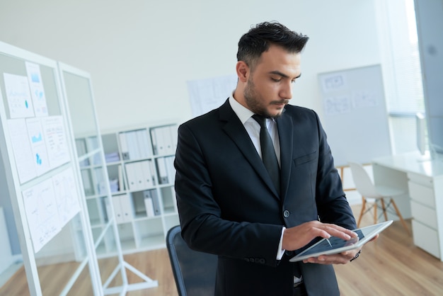 Caucasian businessman in smart suit standing in office and using tablet