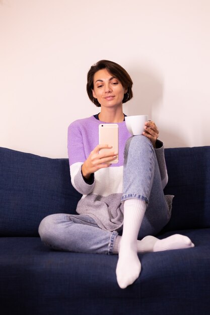 Caucasian cute woman blogger at home in warm purple sweater pullover take selfie in mirror on mobile phone