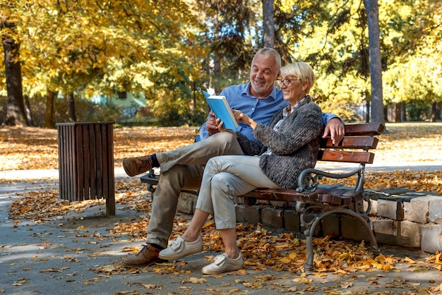 Free photo caucasian elderly couple sitting on a bench and reading a book in the park