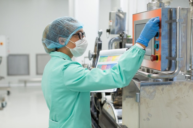 Caucasian factory worker in blue lab suit look at control panel of machine