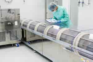 Free photo caucasian factory worker in blue lab suit with tablet in hands bend on manufacture machine check readings