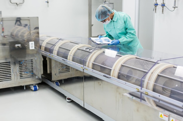 Caucasian factory worker in blue lab suit with tablet in hands bend on manufacture machine check readings