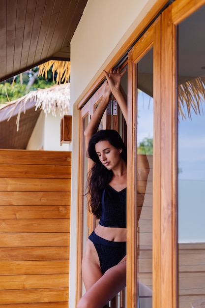 Caucasian fit tanned woman wearing vintage old bikini, posing at luxury hotel villa