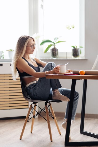 CAucasian freelancer woman work from home. Female hold tea chatting or watching movie use laptop.