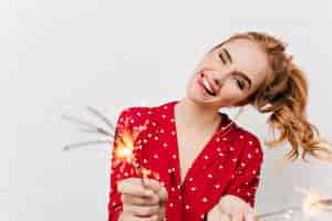 Free photo caucasian girl expressing positive emotions and waving sparklers. wonderful laughing young lady waiting for new year with bengal lights.