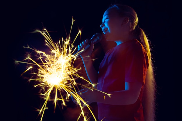 Free photo caucasian girl's portrait on dark studio background in neon light. beautiful female model with speaker and sparkler.