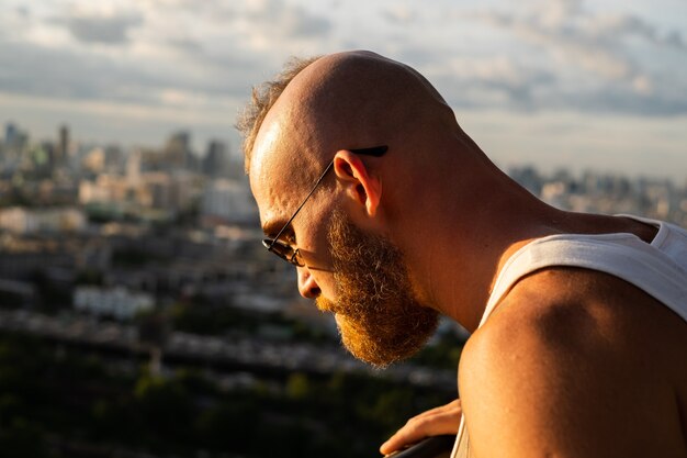 Caucasian handsome bearded brutal man enjoying sunset and view on Bangkok city from high floor