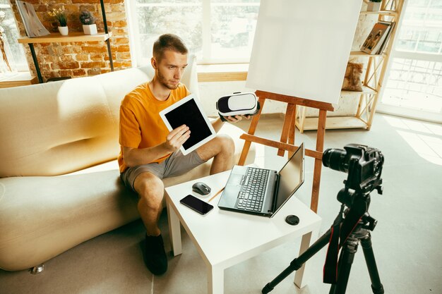 Caucasian male blogger with camera recording video review of gadgets at home