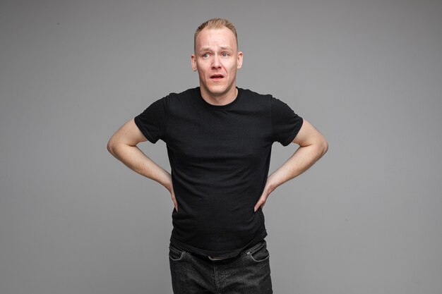 Caucasian male wearing a black t-shirt and jeans posing with hands on a belt isolated on grey wall