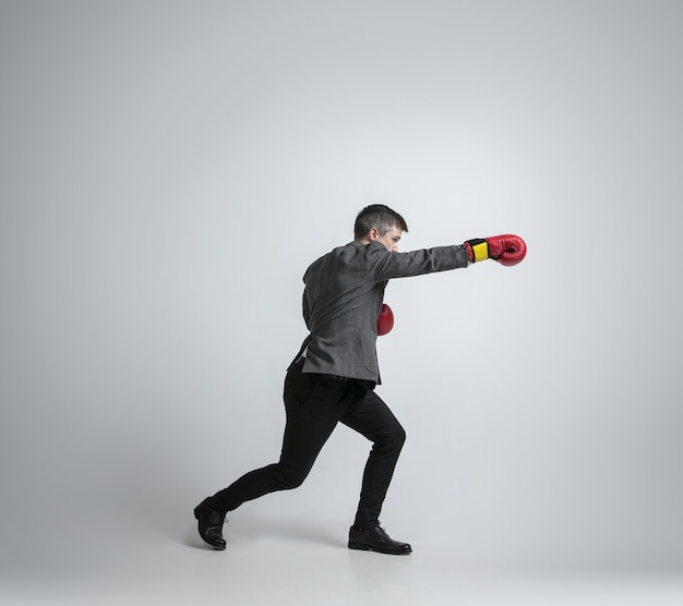 Free Photo caucasian man in office clothes boxing with two red gloves on grey background.