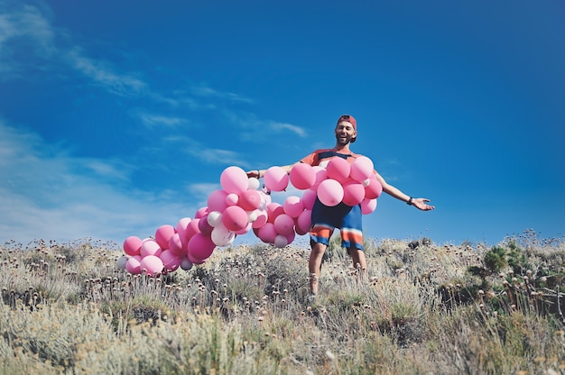 Free photo caucasian man surrounded with a string of pink balloons while standing on a mountain