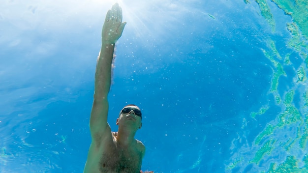 Caucasian man swimming under the water in swimming goggles, blue transparent water