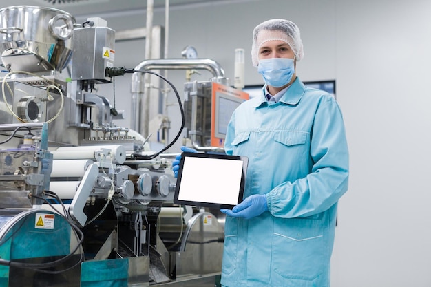 Free Photo caucasian scientist in blue lab uniform stand near manufacture machine with shafts show empty tablet