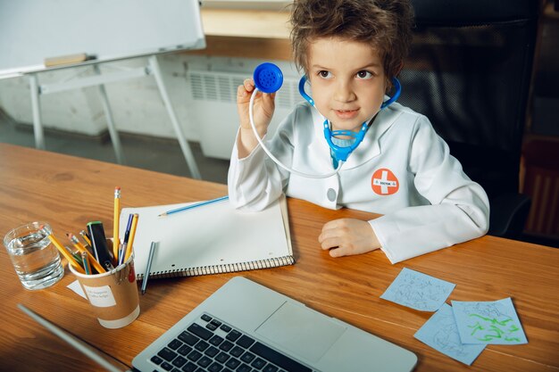 Free photo caucasian teenboy as a doctor consulting for patient, giving recommendation, treating. little doctor during cheking the lungs, listening. concept of childhood, human emotions, health, medicine.