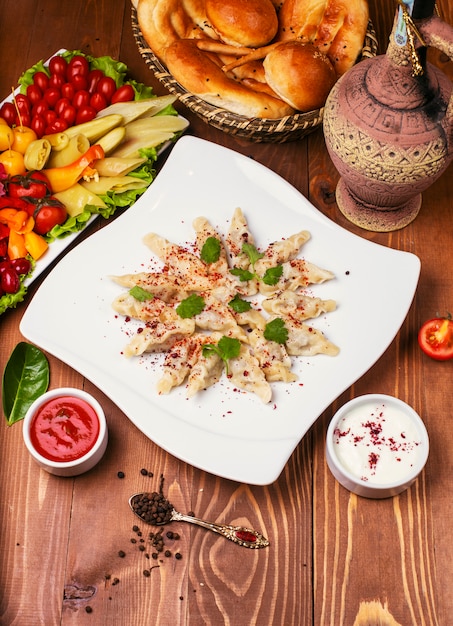 Caucasian traditional foodl dushbere, gurze served with yogurt and tomato sauce. in white plate decorated with turshu on wooden table