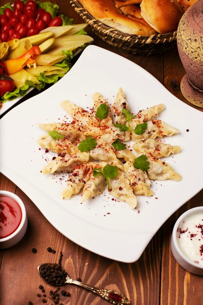 Caucasian traditional foodl dushbere, gurze served with yogurt and tomato sauce. in white plate decorated with turshu on wooden table