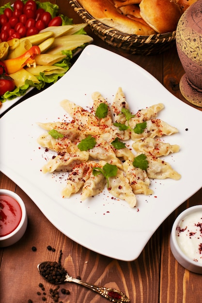 Caucasian traditional foodl dushbere, gurze served with yogurt and tomato sauce. in white plate decorated with turshu on wooden table