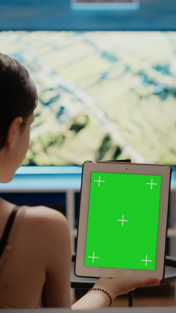 Free photo caucasian woman holding green screen vertically on digital tablet looking at chroma key template and isolated mockup virtual background. young person with modern equipment of copy space