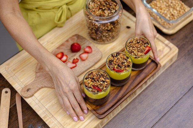 Caucasian woman in kitchen makes chia puddings with mango jam. Desert made of almond milk, chia seeds, cocoa, mango jam and granola.