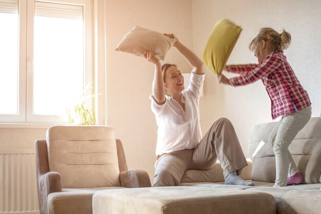 Caucasian woman playing with pillows with her 6-year-old daughter on the couch in their home