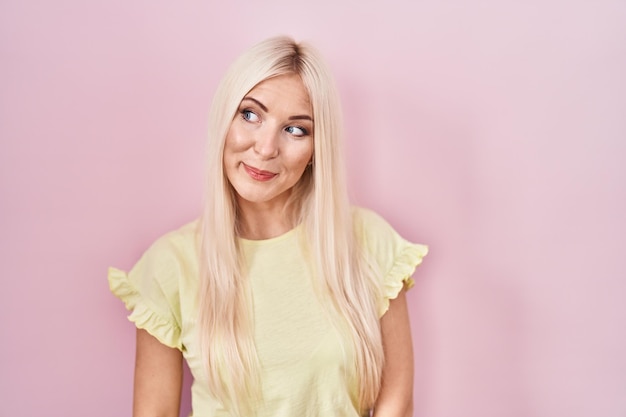 Free photo caucasian woman standing over pink background smiling looking to the side and staring away thinking