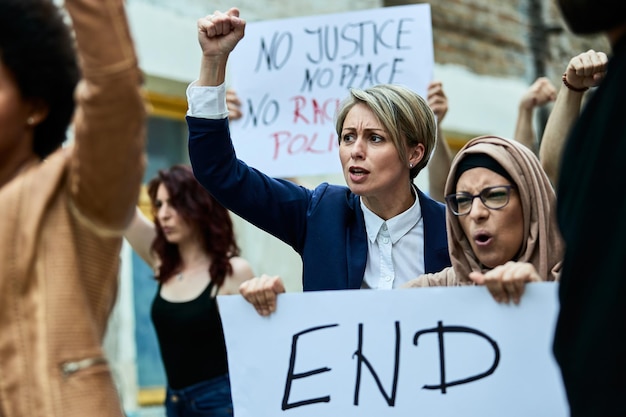 Caucasian woman with raised fist demonstrating with crowd of people against racial discrimination