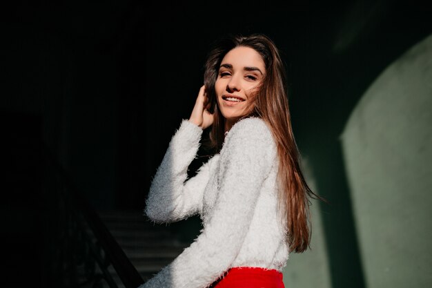 Caucasian woman with straight hair posing near stairs and smiling