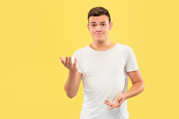 Caucasian young man's half-length portrait on yellow studio background. Beautiful male model in shirt. Concept of human emotions, facial expression, sales, ad. Pointing and showing something.