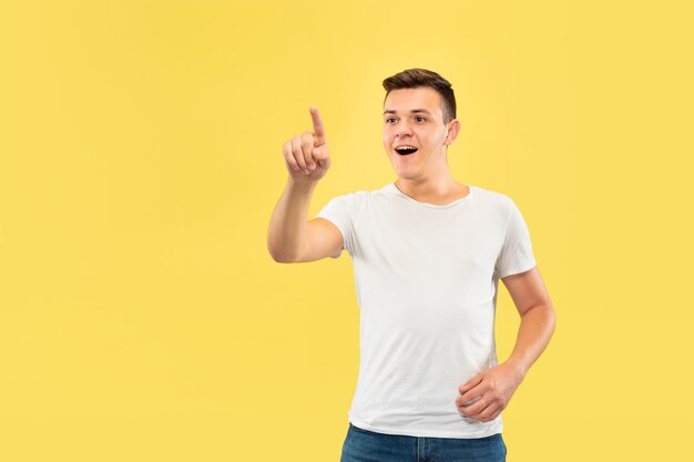 Caucasian young man's half-length portrait on yellow studio background. Beautiful male model in shirt. Concept of human emotions, facial expression, sales, ad. Touching an empty search bar.