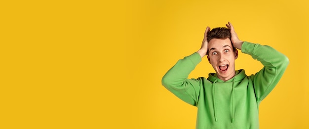 Free photo caucasian young man's portrait on yellow  wall. beautiful male model in green outfit gesturing. concept of human emotions, facial expression, sales, ad, youth. copyspace.