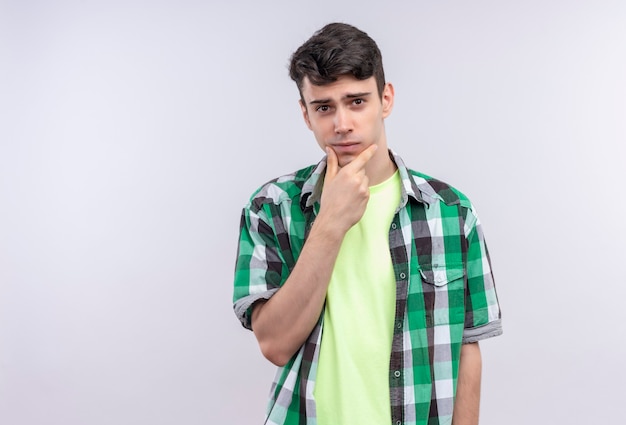 Free photo caucasian young man wearing green shirt put his hand on chin on isolated white wall